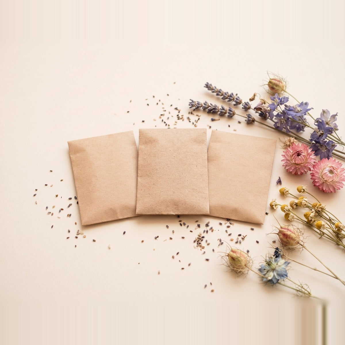 Flower Seeds — a scatter of small mixed flower seeds and three unlabelled plain kraft seed pouches beside a shallow terracotta dish of seeds